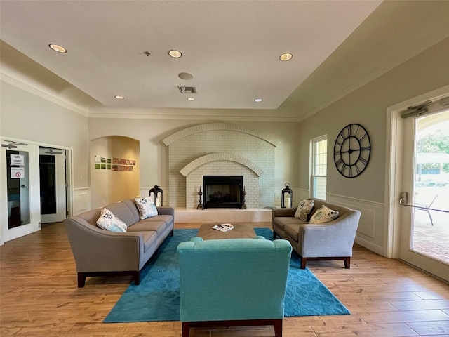 living room featuring light wood-type flooring, ornamental molding, and a brick fireplace