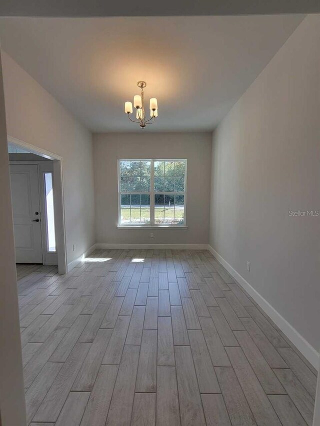 spare room featuring light hardwood / wood-style flooring and a notable chandelier