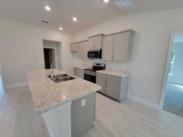 kitchen with light stone countertops, appliances with stainless steel finishes, vaulted ceiling, sink, and a center island with sink