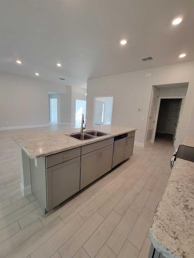 kitchen featuring light stone countertops, sink, light hardwood / wood-style flooring, stainless steel dishwasher, and an island with sink