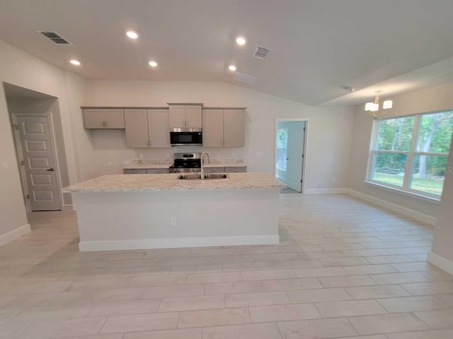 kitchen featuring light stone counters, stainless steel appliances, vaulted ceiling, sink, and an island with sink