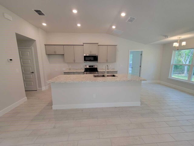 kitchen featuring lofted ceiling, a center island with sink, sink, light stone countertops, and stainless steel appliances