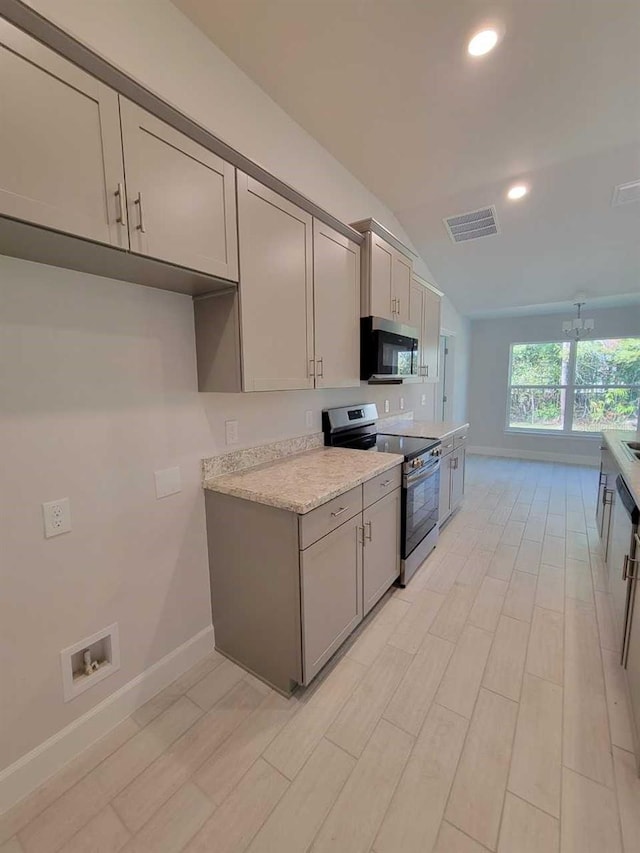 kitchen with lofted ceiling, gray cabinets, light hardwood / wood-style floors, light stone counters, and stainless steel appliances