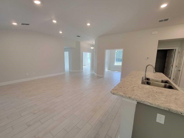 kitchen with light stone countertops, light hardwood / wood-style floors, a kitchen island with sink, and sink