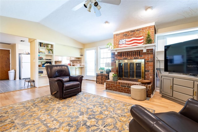 living room featuring hardwood / wood-style floors, vaulted ceiling, ceiling fan, and a brick fireplace