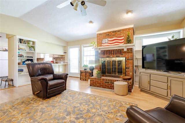 living room featuring lofted ceiling, a brick fireplace, ceiling fan, light wood-type flooring, and a textured ceiling