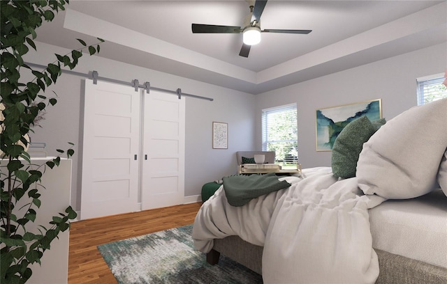 bedroom featuring a barn door, ceiling fan, multiple windows, and hardwood / wood-style flooring