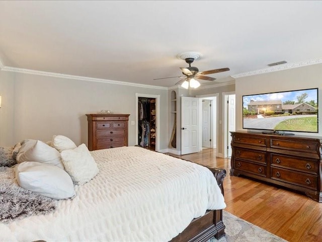 bedroom featuring a spacious closet, ceiling fan, light hardwood / wood-style floors, a closet, and ornamental molding