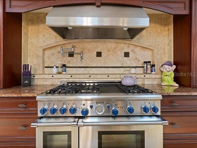 kitchen with decorative backsplash, double oven range, light stone countertops, and extractor fan