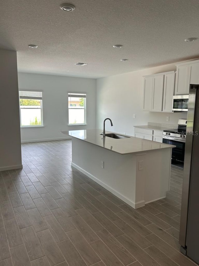 kitchen featuring sink, a textured ceiling, an island with sink, appliances with stainless steel finishes, and white cabinetry