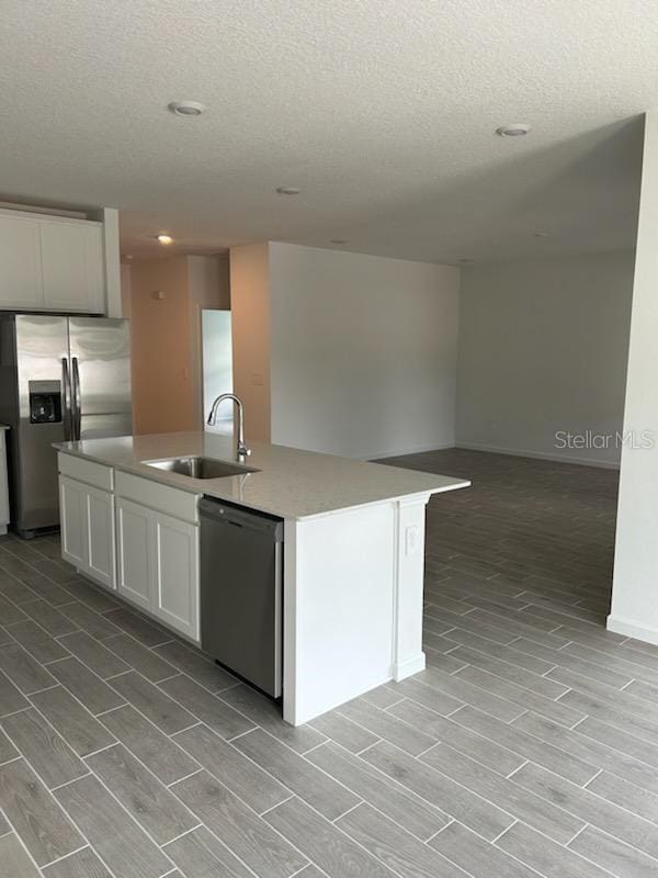 kitchen featuring white cabinetry, sink, stainless steel appliances, an island with sink, and a textured ceiling