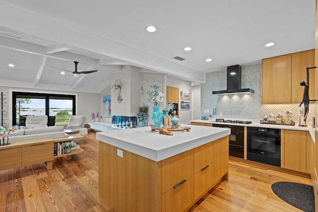 kitchen featuring backsplash, light hardwood / wood-style flooring, wall chimney exhaust hood, black oven, and a kitchen island