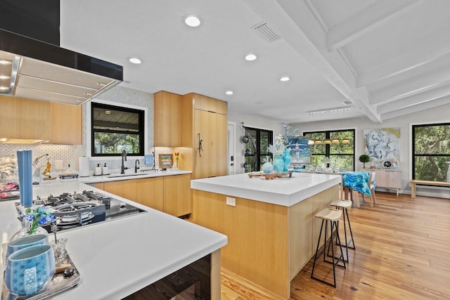 kitchen featuring a center island, sink, beamed ceiling, a breakfast bar area, and extractor fan