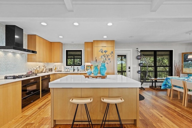 kitchen with a kitchen breakfast bar, black oven, a kitchen island, and wall chimney range hood