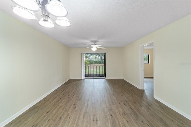 empty room with ceiling fan with notable chandelier, wood-type flooring, and a textured ceiling