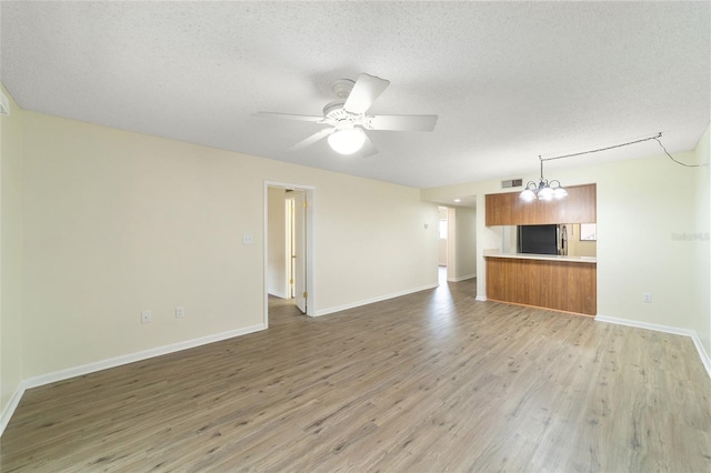 unfurnished living room featuring ceiling fan with notable chandelier, a textured ceiling, and hardwood / wood-style flooring