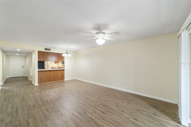 unfurnished living room featuring ceiling fan with notable chandelier, a textured ceiling, and hardwood / wood-style flooring