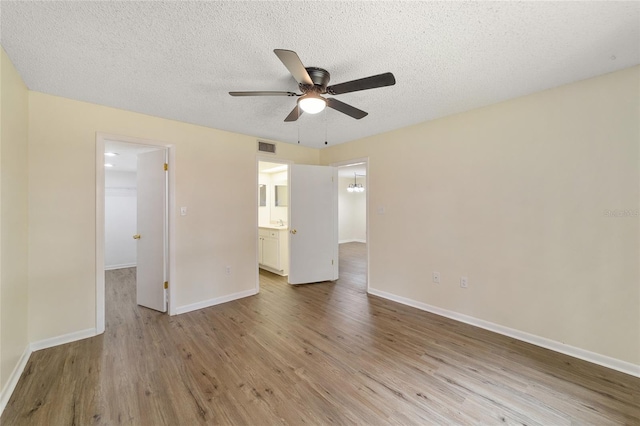 unfurnished bedroom with ensuite bath, a textured ceiling, ceiling fan, hardwood / wood-style flooring, and a spacious closet