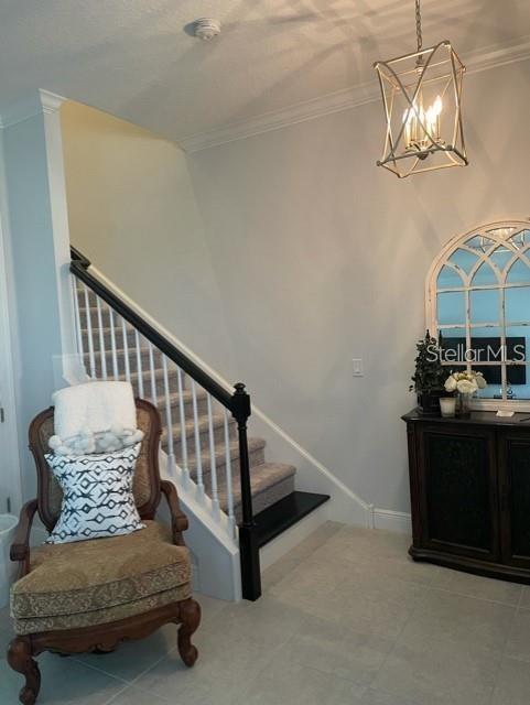 stairway featuring a notable chandelier, ornamental molding, and light tile floors