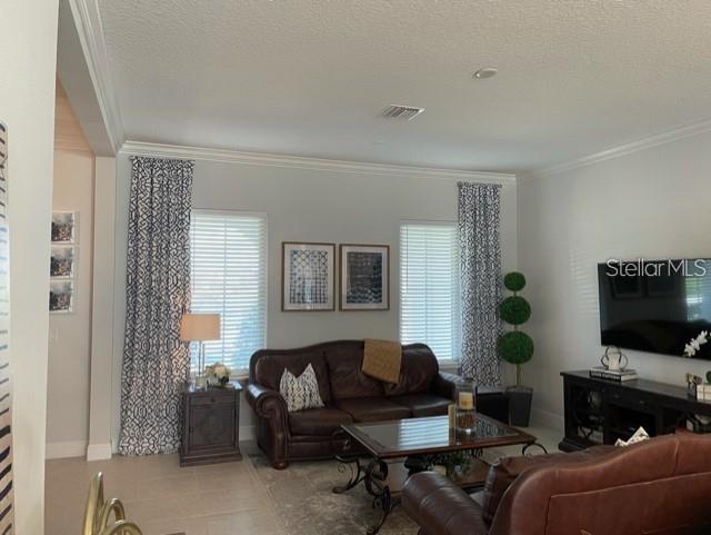 living room with light tile flooring, a textured ceiling, and crown molding