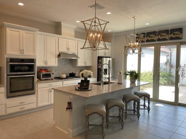 kitchen with a center island with sink, appliances with stainless steel finishes, white cabinets, pendant lighting, and sink