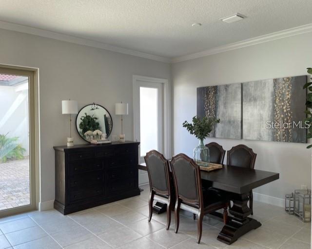 dining room with a textured ceiling, crown molding, and light tile flooring