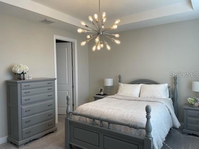 carpeted bedroom with an inviting chandelier and a tray ceiling