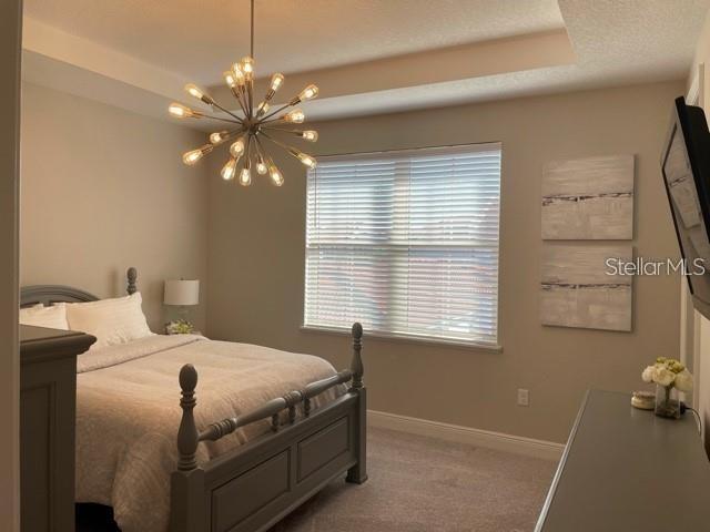 bedroom featuring a raised ceiling, carpet floors, and a chandelier