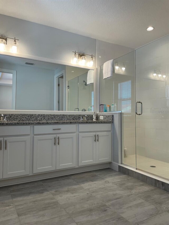 bathroom featuring double sink, a shower with door, a textured ceiling, and large vanity