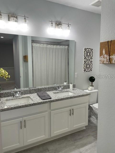 bathroom featuring dual bowl vanity and toilet