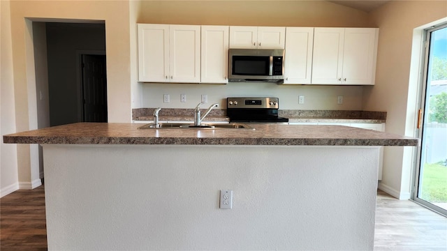 kitchen with wood-type flooring, range, sink, a kitchen island with sink, and white cabinetry