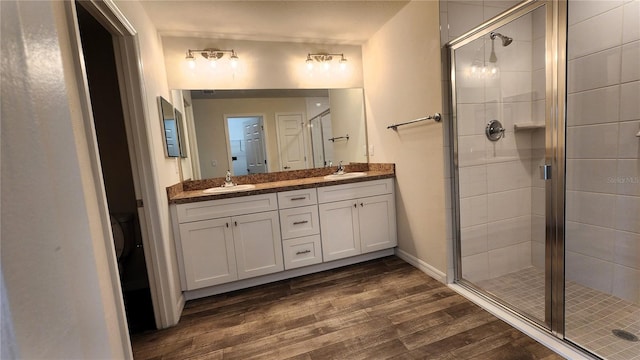 bathroom featuring wood-type flooring, vanity with extensive cabinet space, walk in shower, and dual sinks