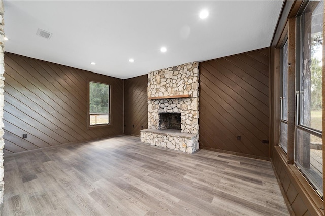 unfurnished living room with a fireplace, light hardwood / wood-style flooring, and wood walls