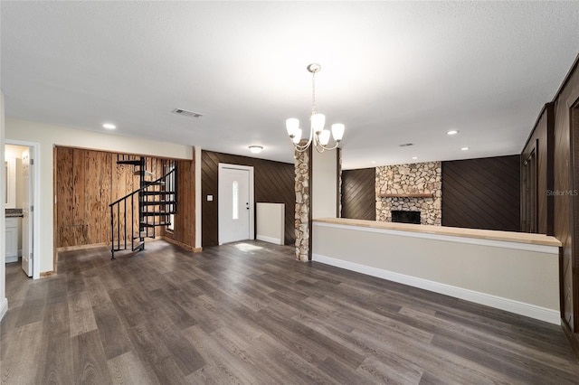 unfurnished living room featuring dark hardwood / wood-style flooring, an inviting chandelier, a stone fireplace, and wood walls