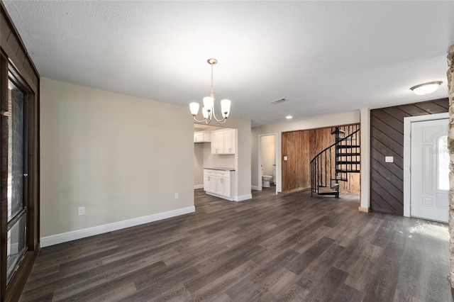 unfurnished living room with a textured ceiling, a notable chandelier, wood walls, and dark hardwood / wood-style floors