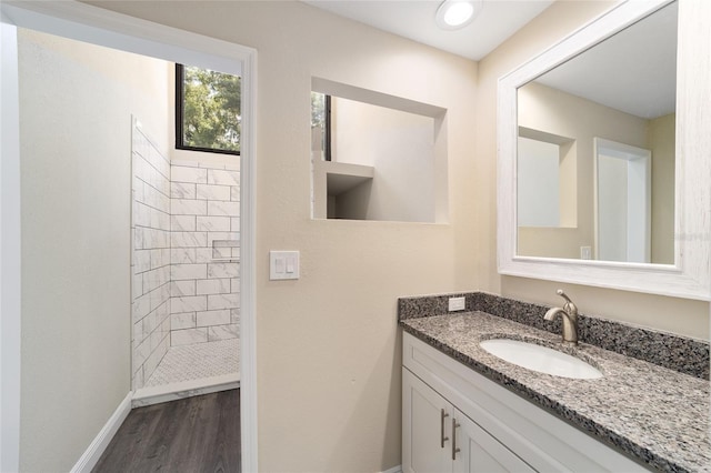 bathroom with hardwood / wood-style flooring, vanity, and tiled shower