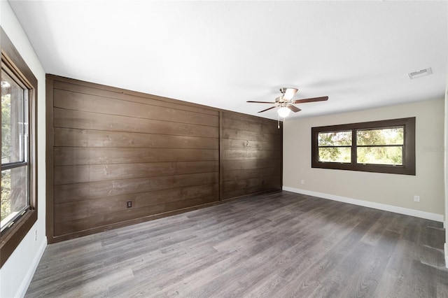 spare room featuring dark hardwood / wood-style floors, ceiling fan, and wood walls