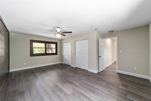 unfurnished bedroom featuring two closets, ceiling fan, and dark wood-type flooring