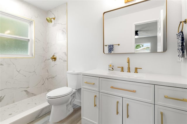 bathroom featuring toilet, tiled shower, ceiling fan, wood-type flooring, and vanity