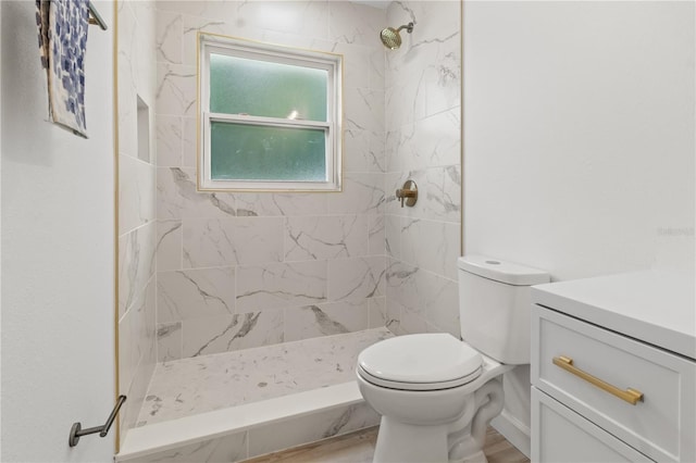 bathroom featuring toilet, a tile shower, wood-type flooring, and vanity