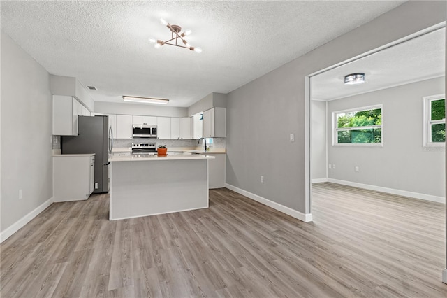 kitchen featuring white cabinets, light wood-type flooring, appliances with stainless steel finishes, and a textured ceiling