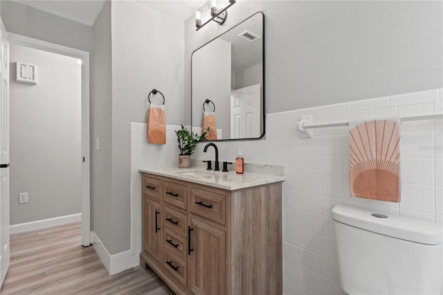 bathroom with toilet, hardwood / wood-style flooring, tile walls, and vanity