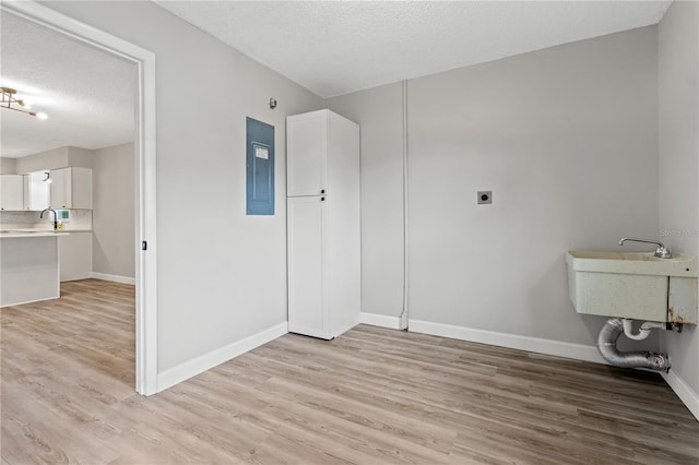 washroom with sink, a textured ceiling, electric dryer hookup, electric panel, and light wood-type flooring