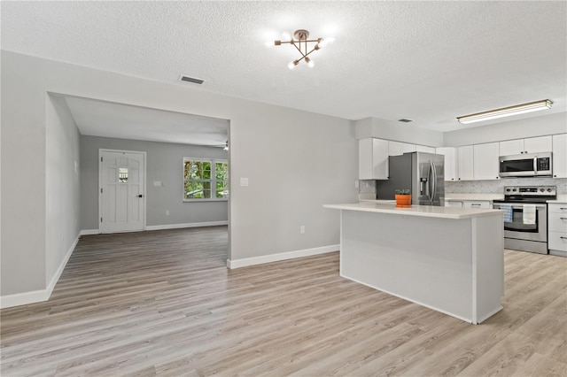 kitchen with a textured ceiling, light wood-type flooring, backsplash, white cabinets, and appliances with stainless steel finishes