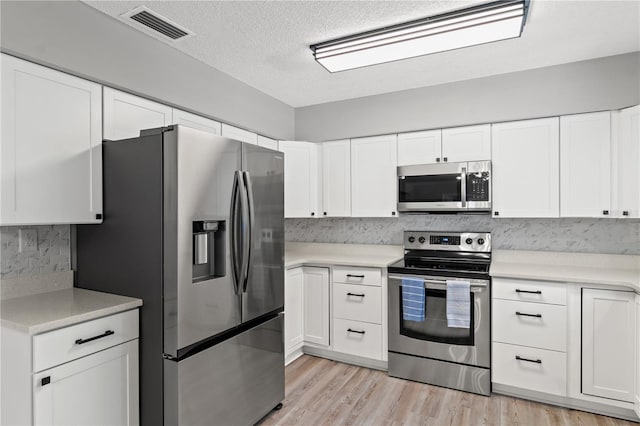 kitchen with stainless steel appliances, white cabinets, a textured ceiling, light hardwood / wood-style flooring, and backsplash