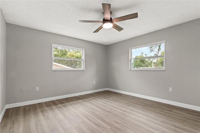 empty room with a textured ceiling, ceiling fan, light hardwood / wood-style floors, and a healthy amount of sunlight