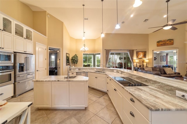 kitchen featuring a towering ceiling, decorative light fixtures, stainless steel appliances, ceiling fan with notable chandelier, and a center island with sink