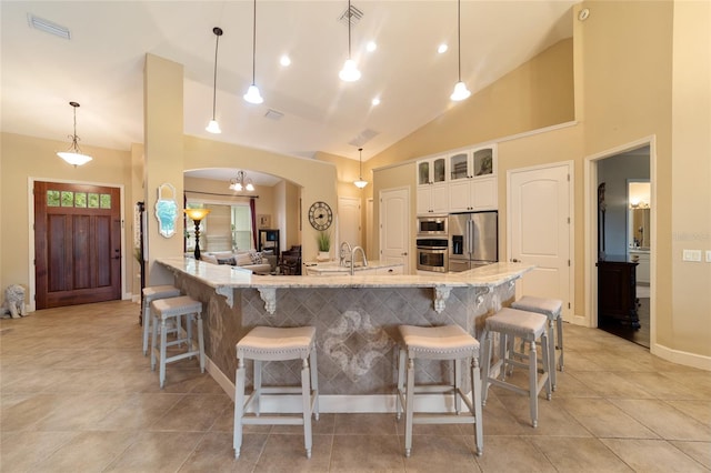 kitchen featuring hanging light fixtures, white cabinets, light stone counters, high vaulted ceiling, and stainless steel appliances