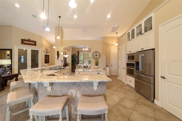 kitchen with appliances with stainless steel finishes, decorative light fixtures, light stone countertops, a kitchen bar, and lofted ceiling