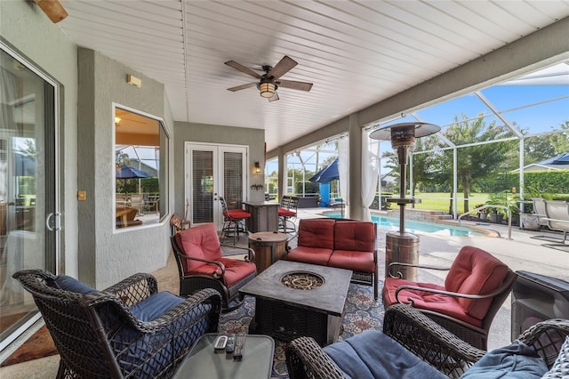 view of patio with ceiling fan, glass enclosure, french doors, and an outdoor living space with a fire pit